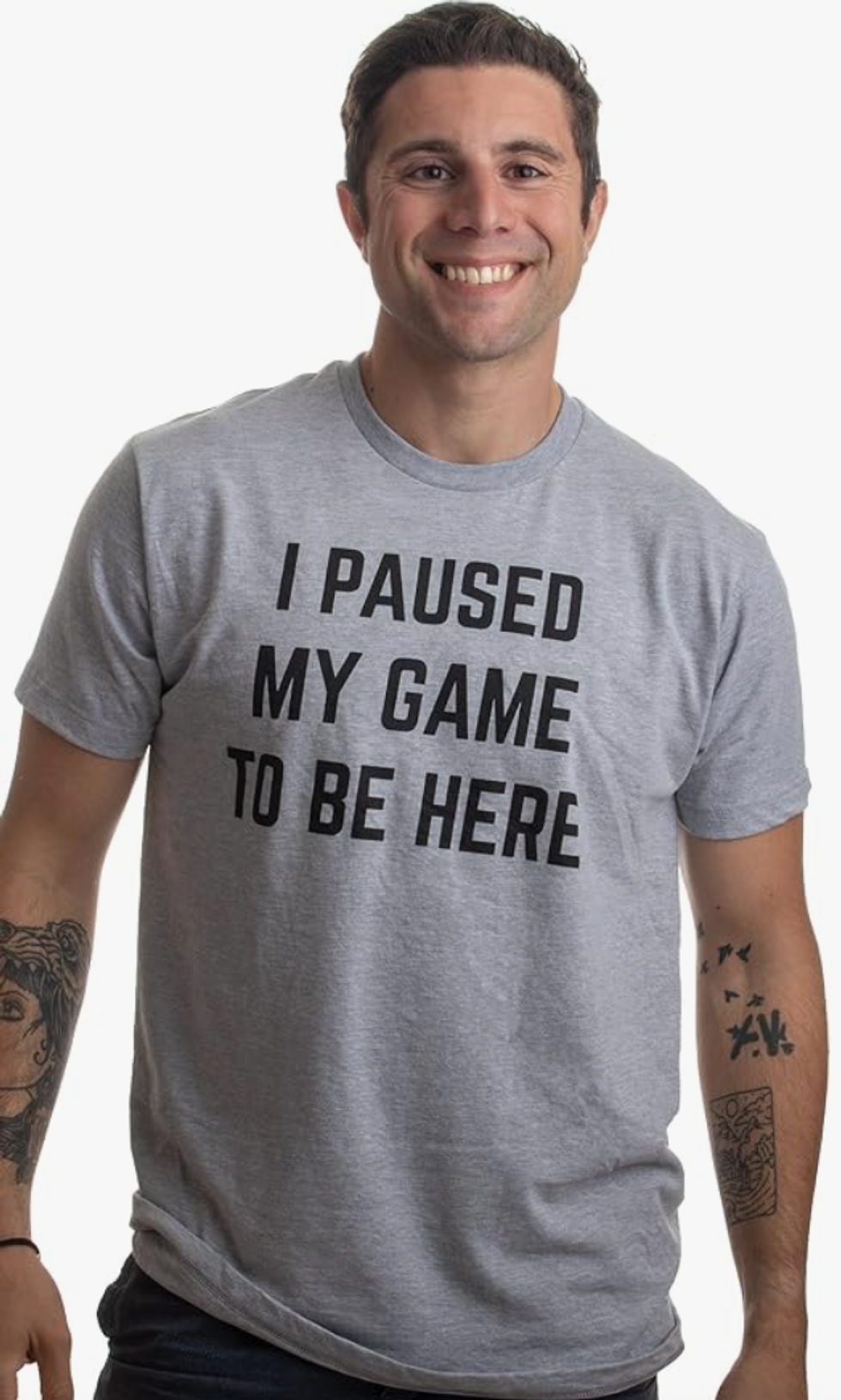 A smiling man wearing a grey T-shirt that says "I paused my game to be here."