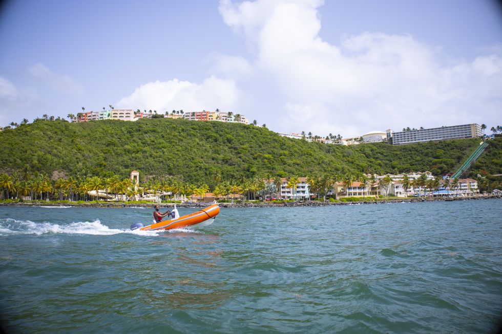 A speed boat accelerates past a forested coastline dotted with colourful buildings and palm trees near Fajardo, Puerto Rico.