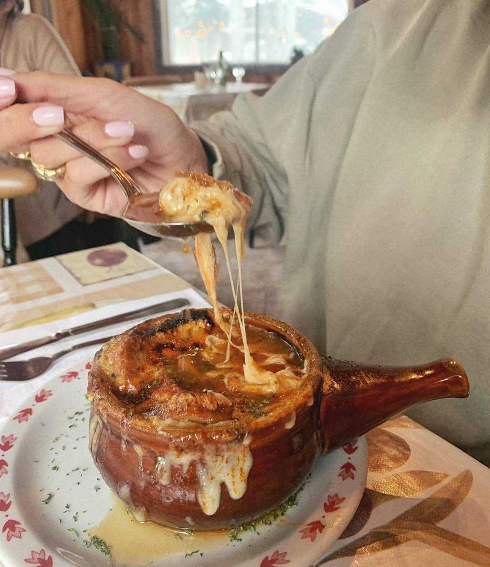 A spoonful of French onion soup in a brown bowl.