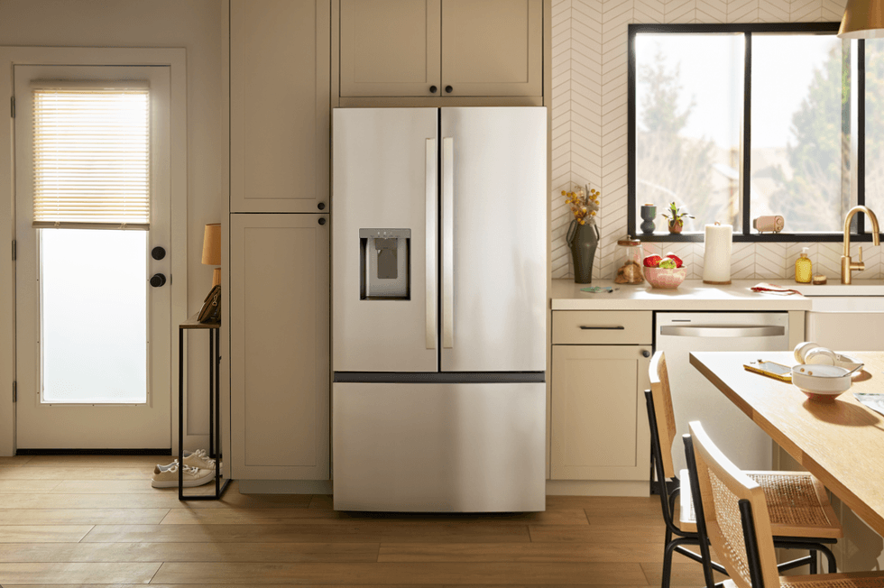 A stainless steel French door refrigerator with a bottom freezer in a bright, modern kitchen with neutral cabinetry and natural light.