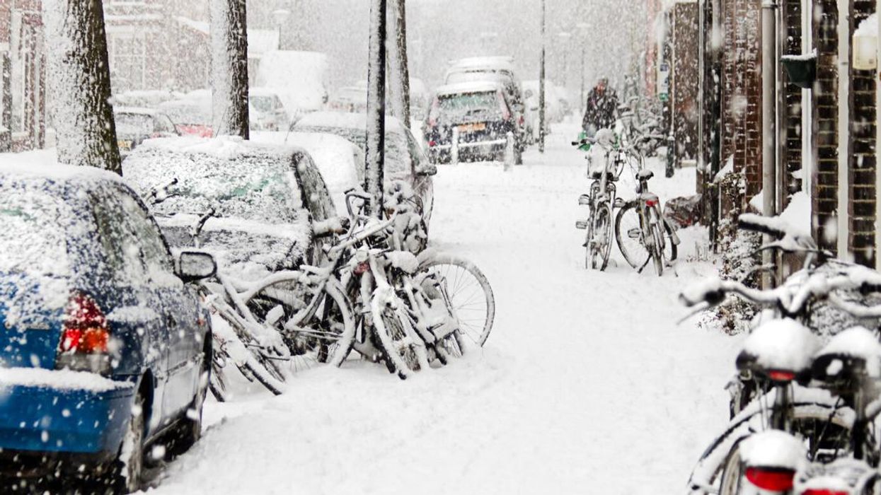 A street of cars and bikes covered in snow.