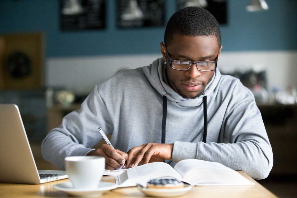A student at a desk with a laptop, taking notes from a textbook.