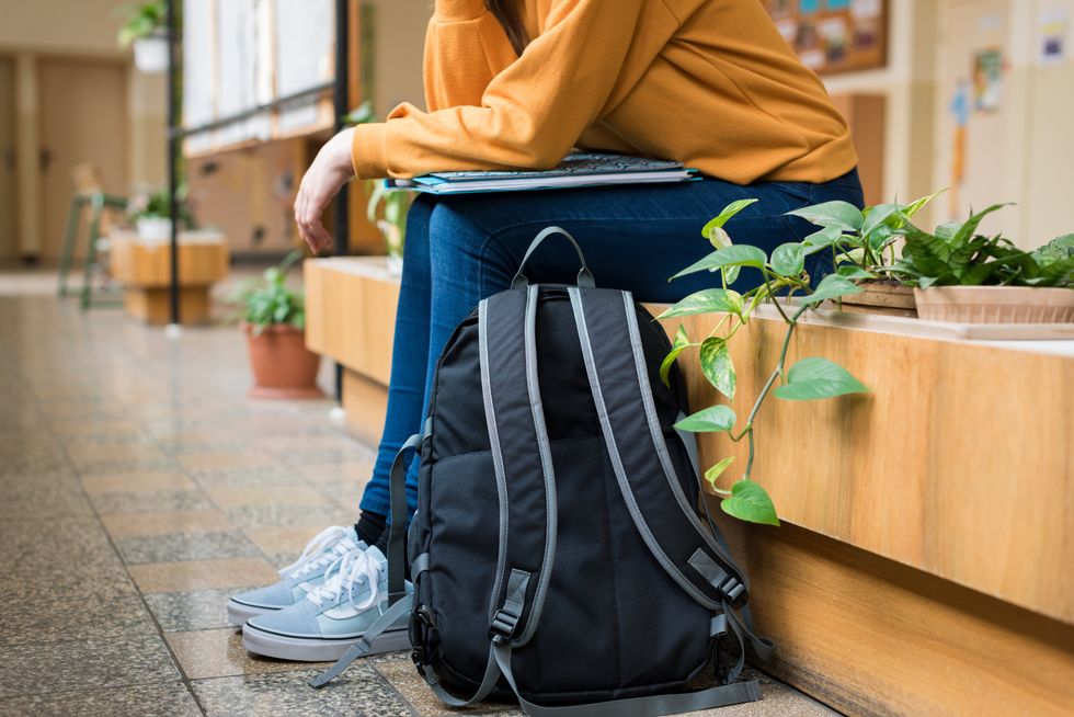 A student sitting in an empty hallway with their backpack on the ground.