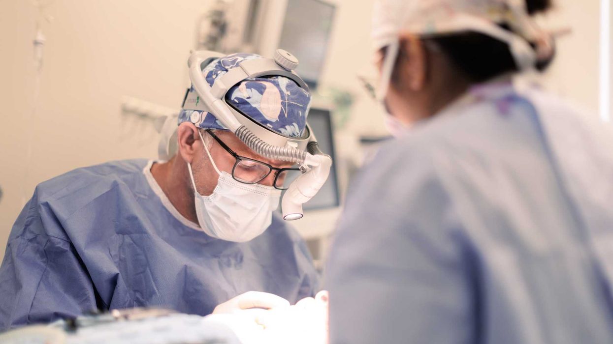 A surgeon in scrubs performs surgery with the help of a nurse.