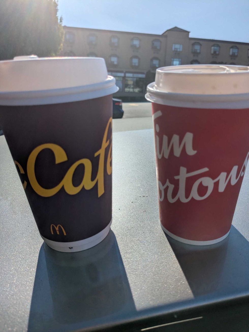 A Tim Hortons and McDonald's coffee cup side by side on top of a car