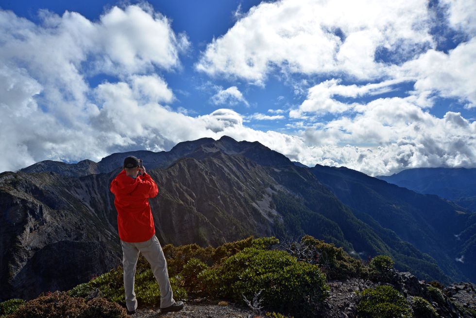 A traveller in a red jacket takes a photo of mountains in Taiwan. 