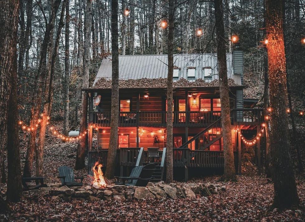 A two-storey wooden house stands in the woods of Georgia surrounded by trees and patio lights.