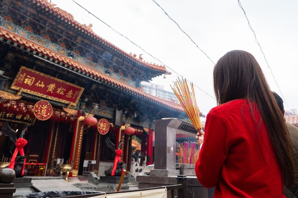 A visitor wearing red makes and incense offering at a temple.