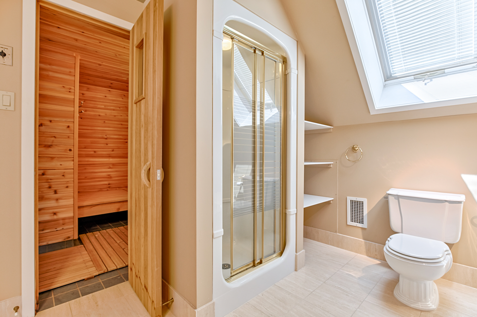 A washroom that has a wooden sauna, shower with glass doors and a white toilet.