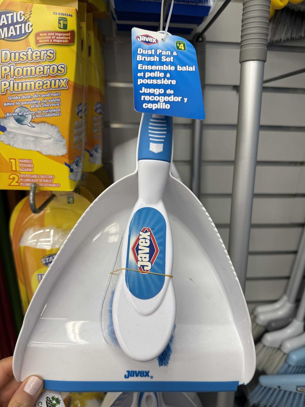A white and blue dust pan attached to a brush hanging on a store shelf.