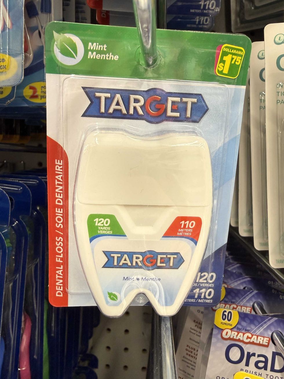 A white, blue and green pack of dental floss on a store shelf.