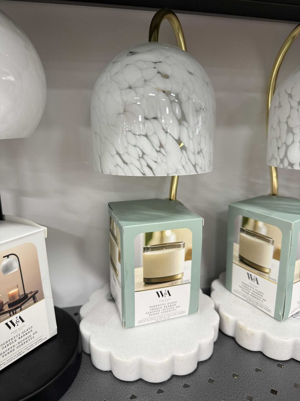 A white lamp looking item on a store shelf that has a label with a picture of a candle on it and reads glass candle warmer.