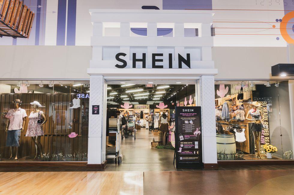 A white shop front of a fashion store with outfits in the window and SHEIN over the doorway.