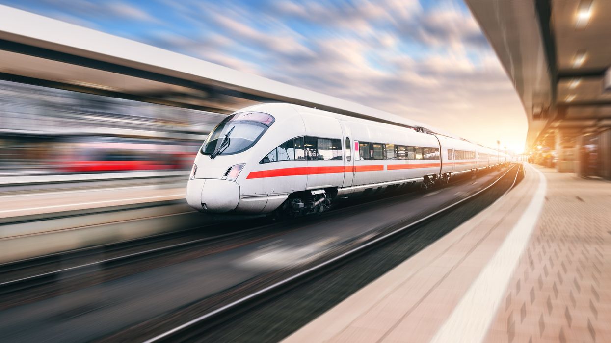 A white train speeds through an unnamed station.