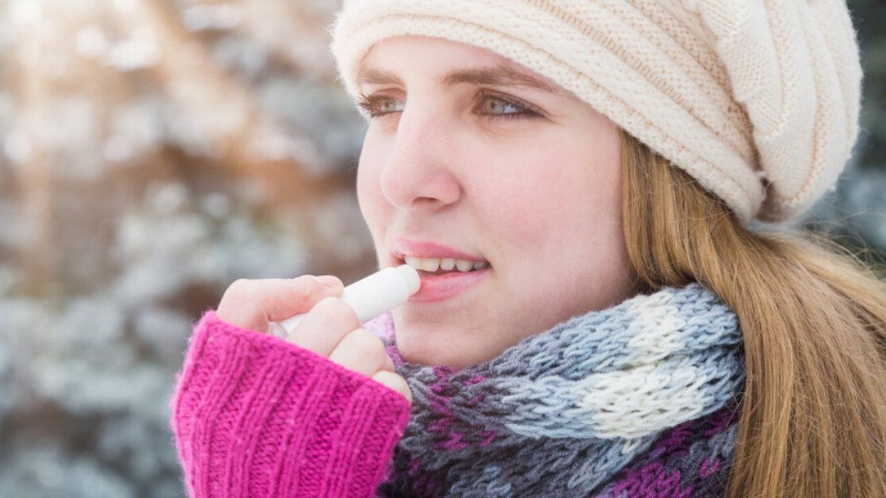 A woman bundled up in a hat and scarf is applying lip balm on a cold day.