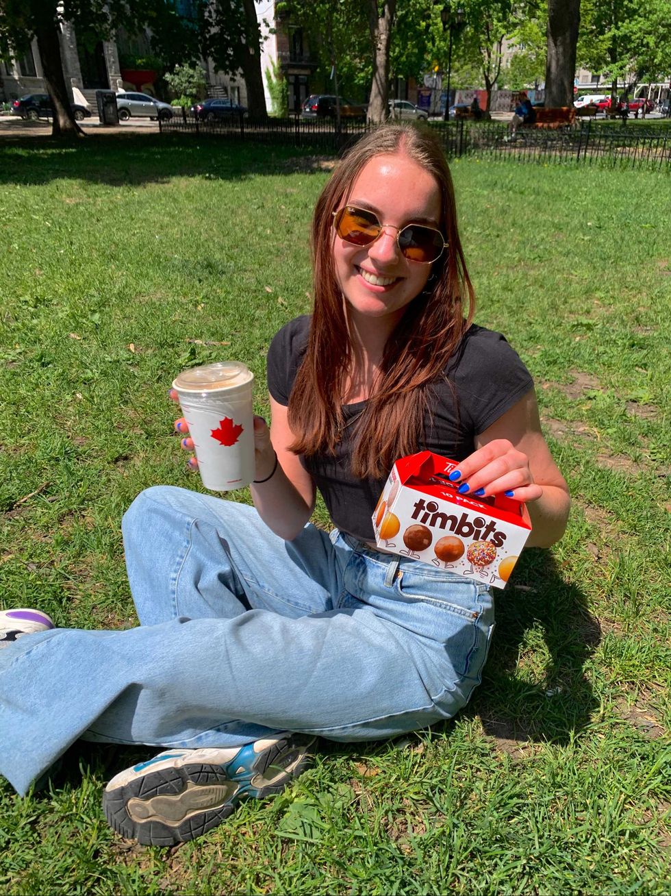 A woman holding a box of TimBits and a coffee.