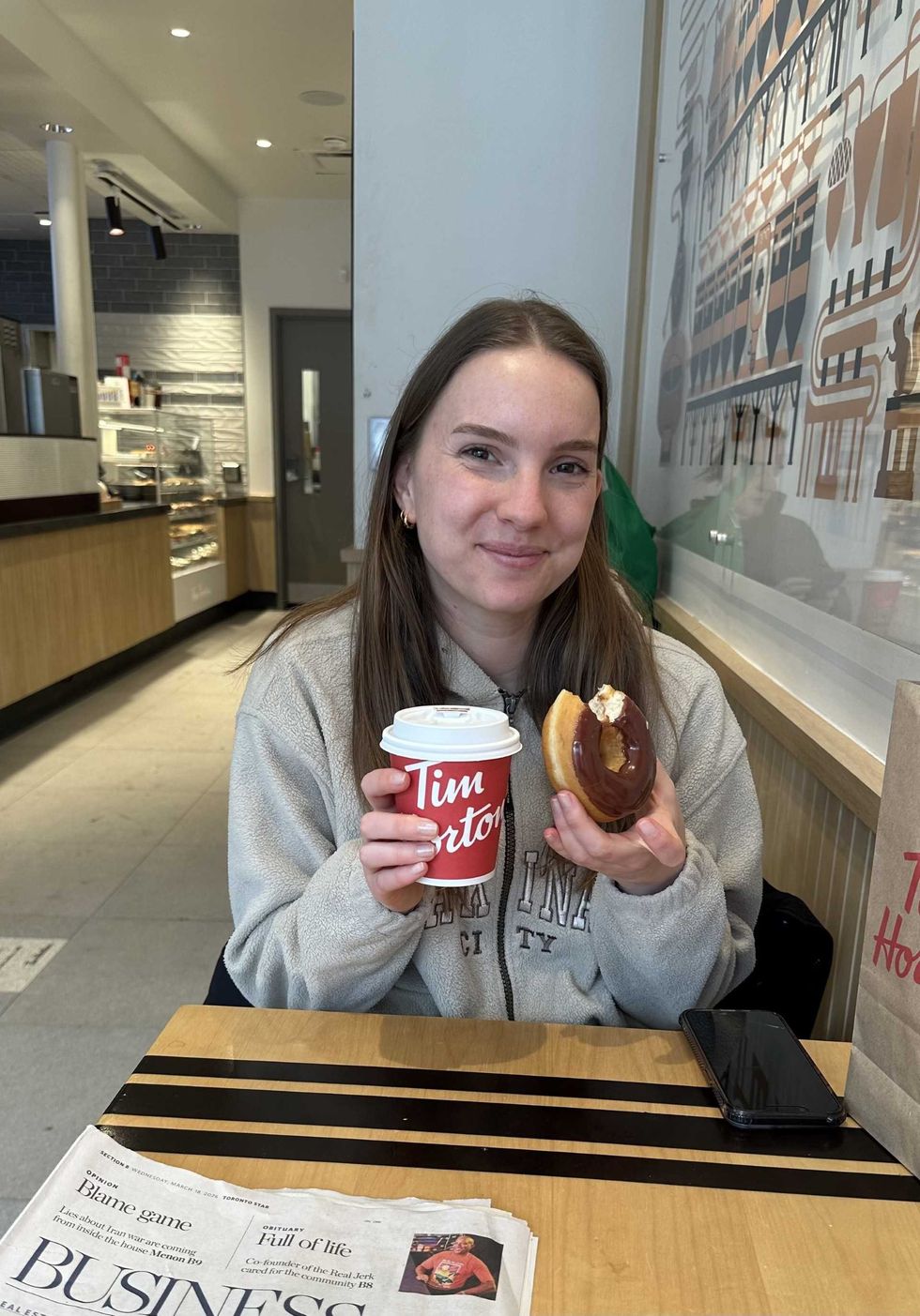 A woman holding a donut and Tim Hortons coffee cup.
