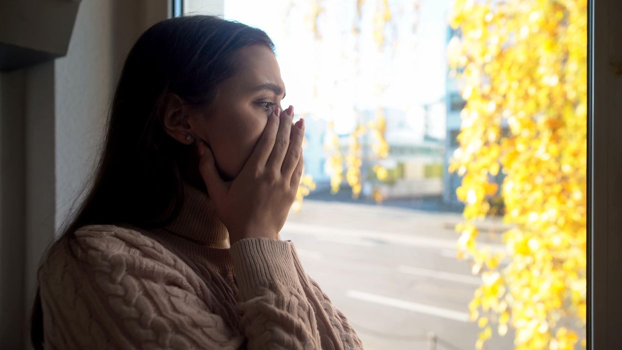 A woman holding her face while looking out a window.