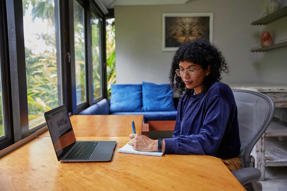A woman in a blue sweater sitting at a table with a laptop.