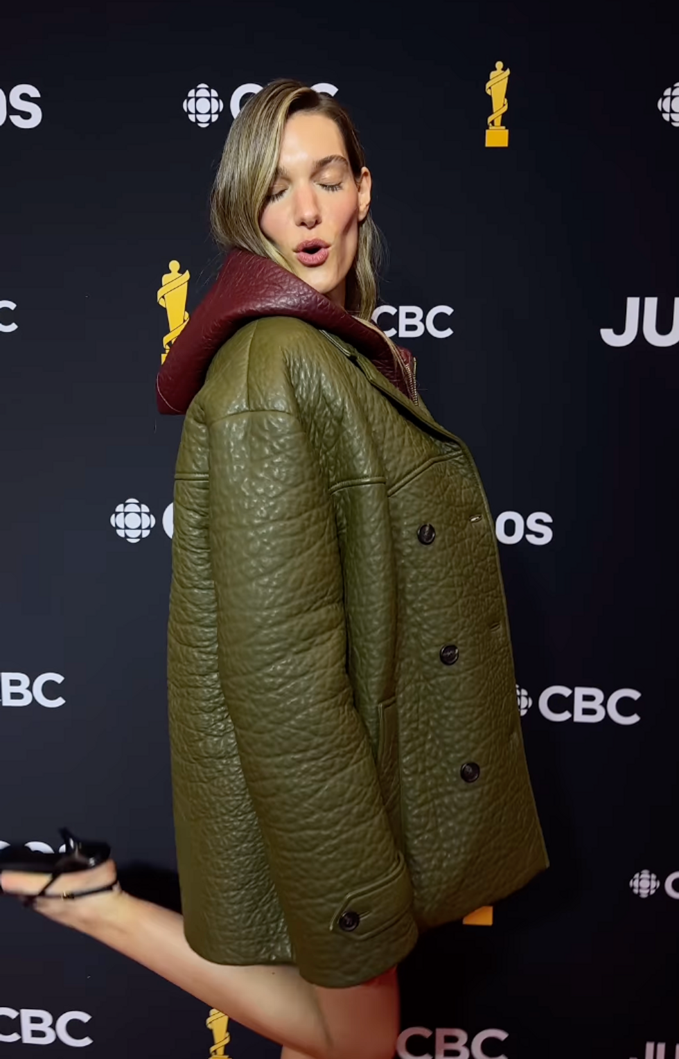 A woman in a green jacket blowing a kiss for the camera.