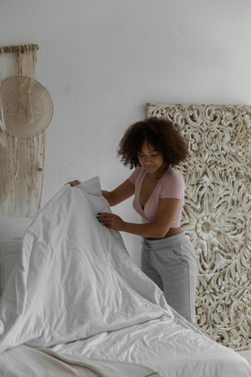 A woman in comfortable clothes changes bedsheets.