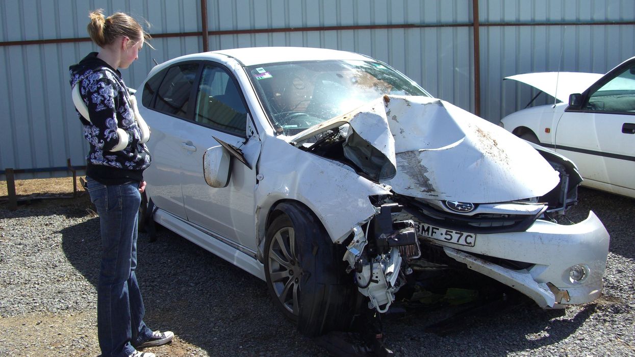A woman looking at a crashed car.