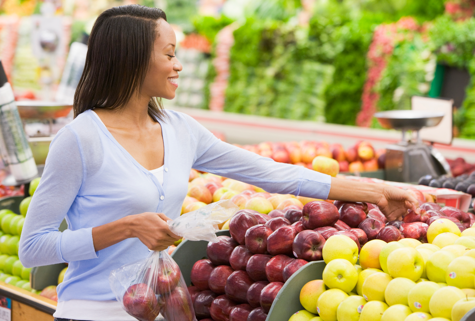 A woman picking up a red apple to buy at a grocery store.
