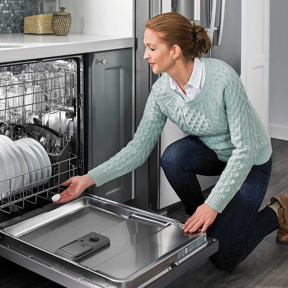 A woman puts a dishwasher cleaner tablet in the bottom of a dishwasher.