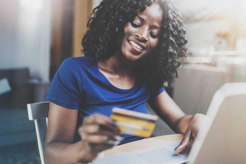 A woman sitting at a table looks at a credit card while using a laptop.