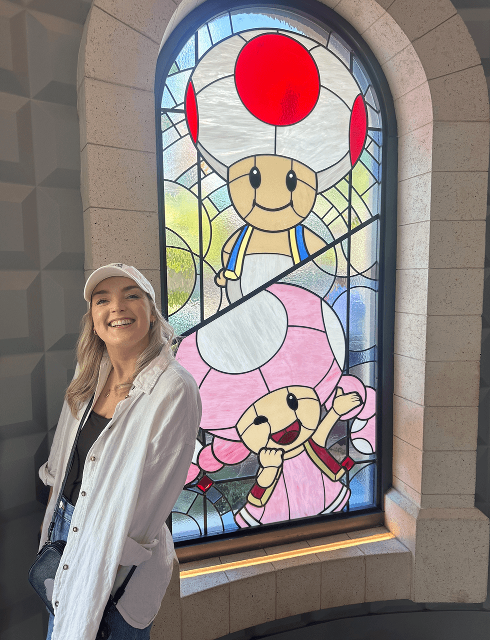 A woman smiling in front of a large stained glass window depicting Toad and Toadette from the Super Mario franchise.
