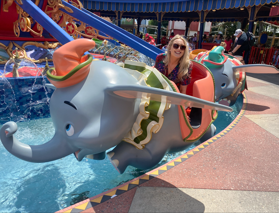 A woman smiling while riding the Dumbo the Flying Elephant ride.