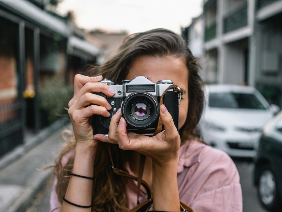 A woman takes a photo using an SLR camera on a quiet street.