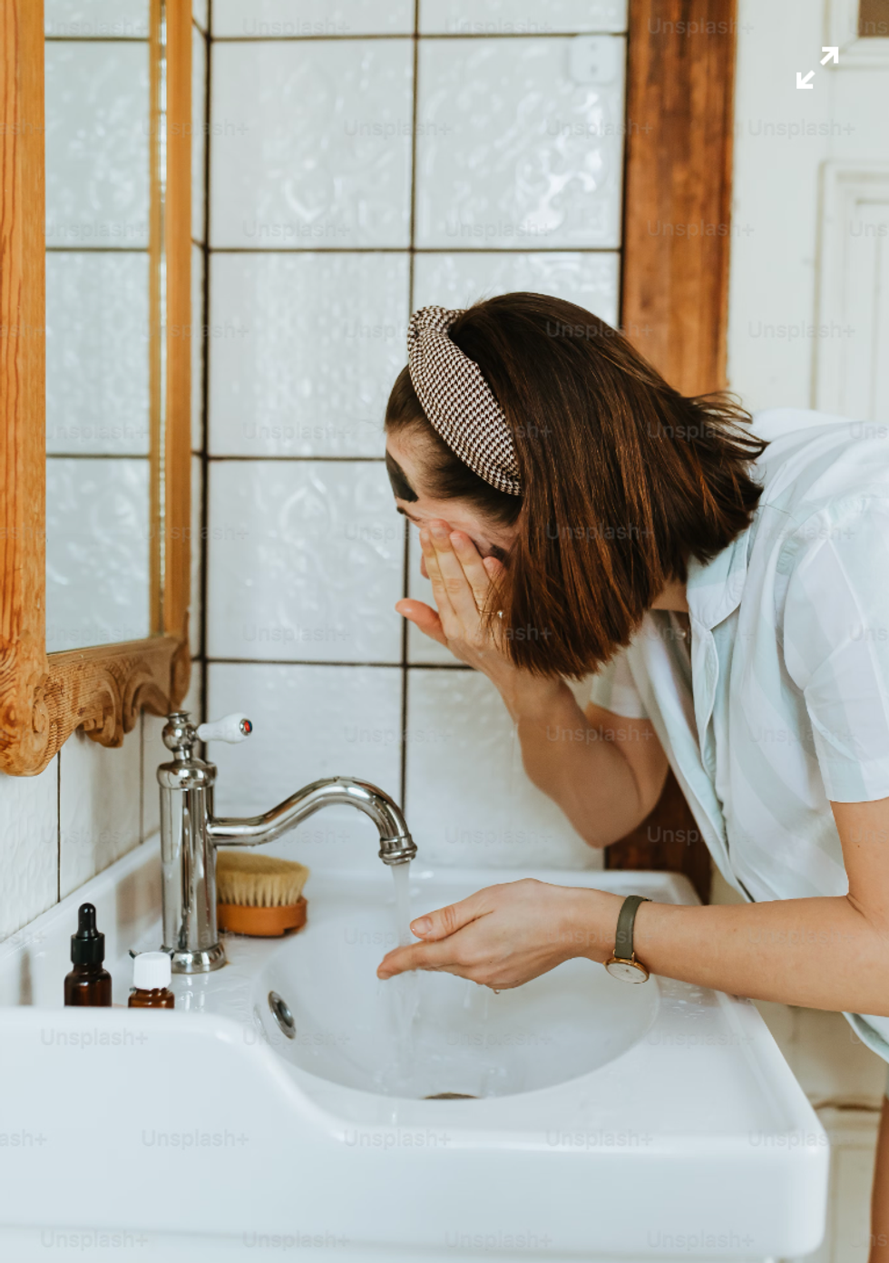 A woman washing her face in the bathroom sink.