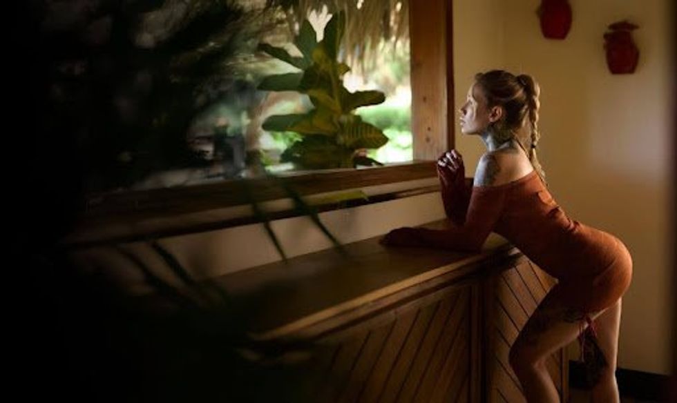 A woman wearing a short, off-the-shoulder dress looks out a window.