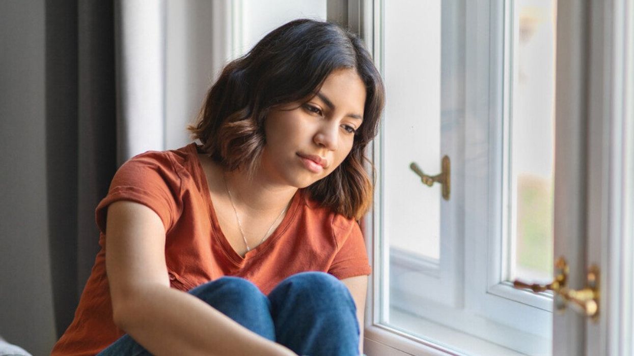 A woman who looks sad sitting by the window.