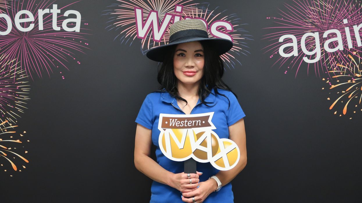 A woman with dark hair stands in front of a backdrop that reads "Alberta wins again" holding a sign reading "Western MAX."