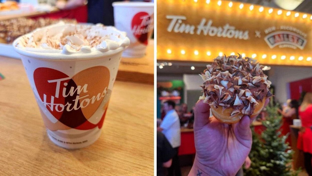 A wooden table with a white Tim Hortons cup with white whipped cream topping and brown sprinkles. A hand holding a doughnut with white and brown chocolate flakes and brown chocolate icing.