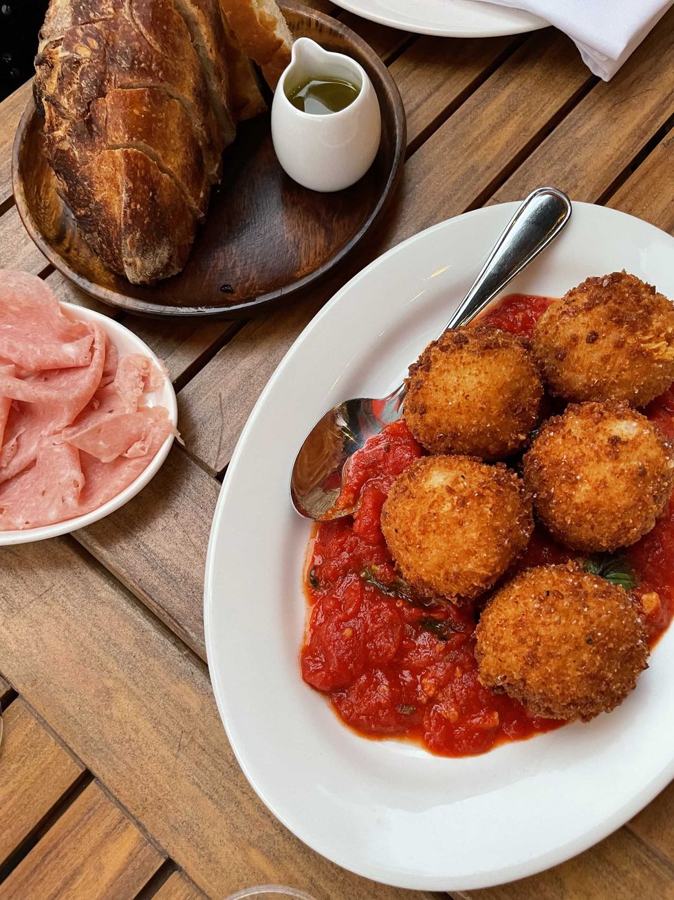 A wooden tabletop with a plate of mortadella, a plate of arancini, and fresh bread with olive oil.