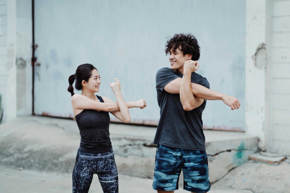 A young woman and man stretching their arms together.