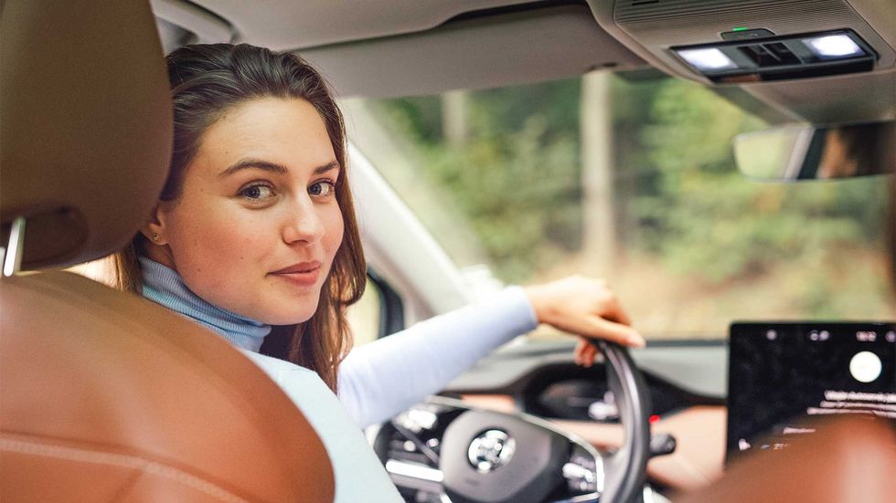  A young woman looks back over her shoulder from the driver's seat of a luxury car. 