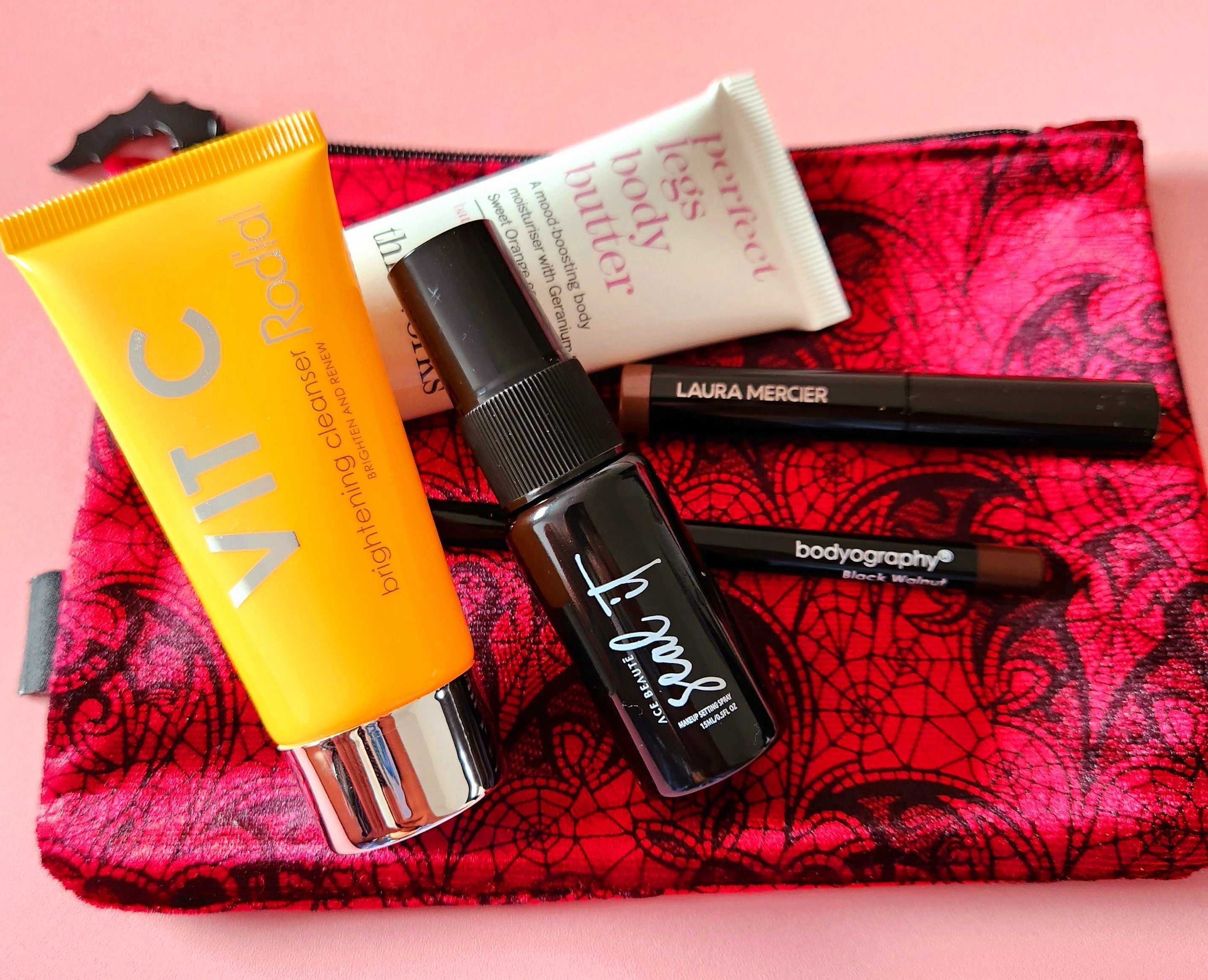 Ace Beaute - Seal It Setting Spray, Bodyography - Eye Pencil, Laura Mercier - Caviar Stick Mini, This Works - Perfect Legs Body Butter and Rodial - Vit C Brightening Cleanser on a red and cobweb makeup b ag.