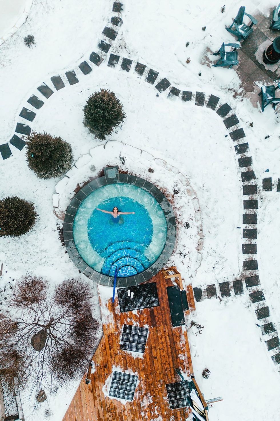 An aerial view of a hot tub surrounded by snow at Terra Nova Nordic Spa with a guest floating on their back in the water.