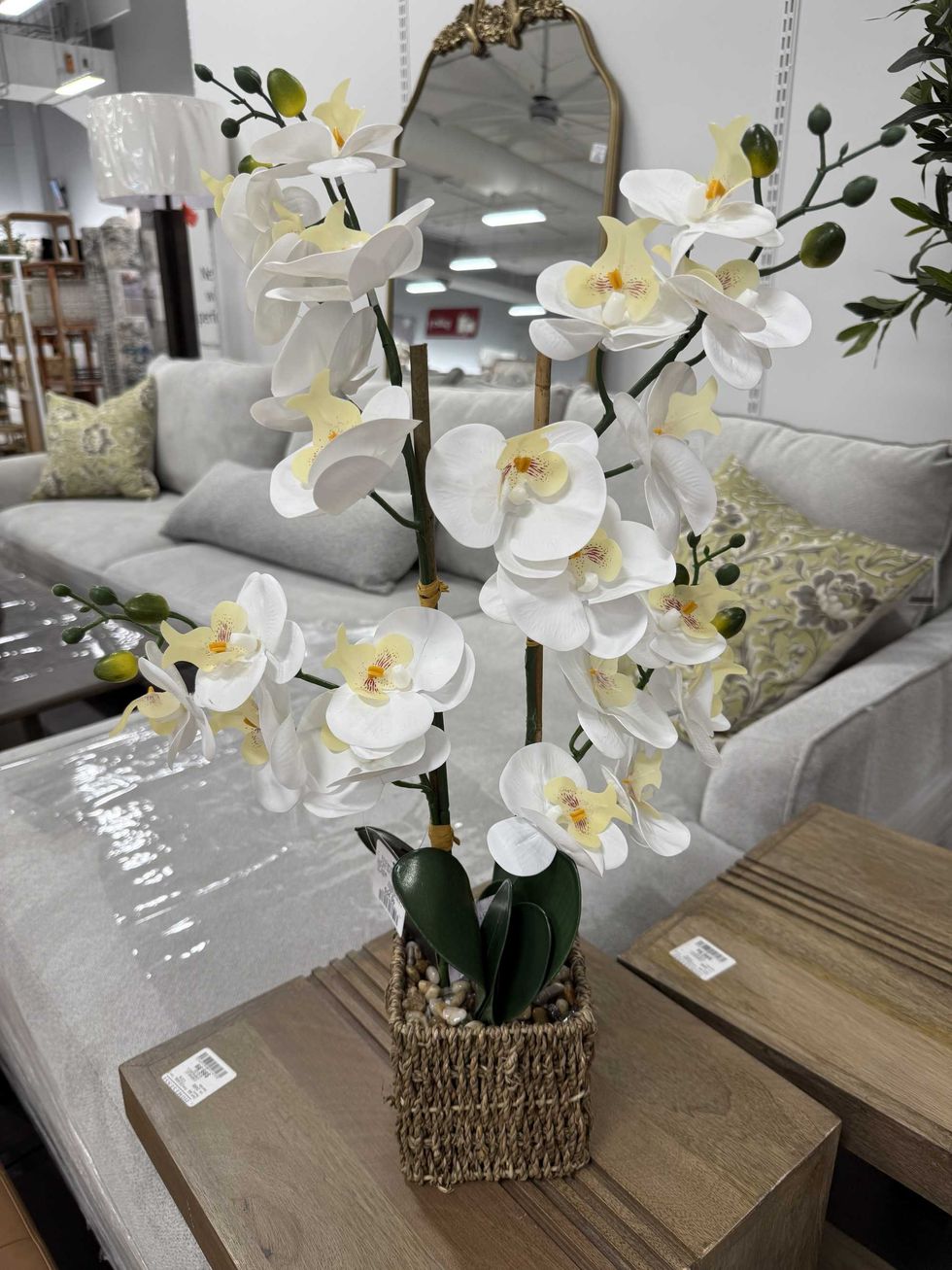 An artificial white orchid in a wicker basket with small rocks at the base.