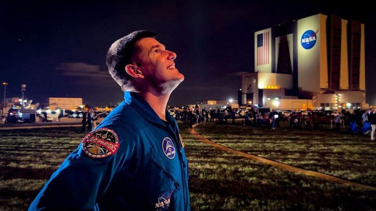 An astronaut in uniform looking up at night with a NASA building in the background.