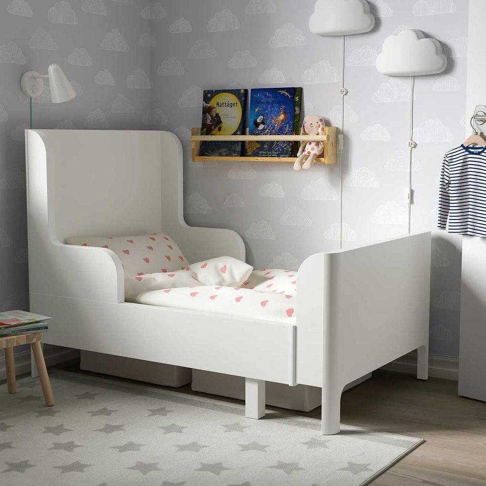 An extendable child's bed in a befroom with cloud wallpaper and a rug patterned with stars.