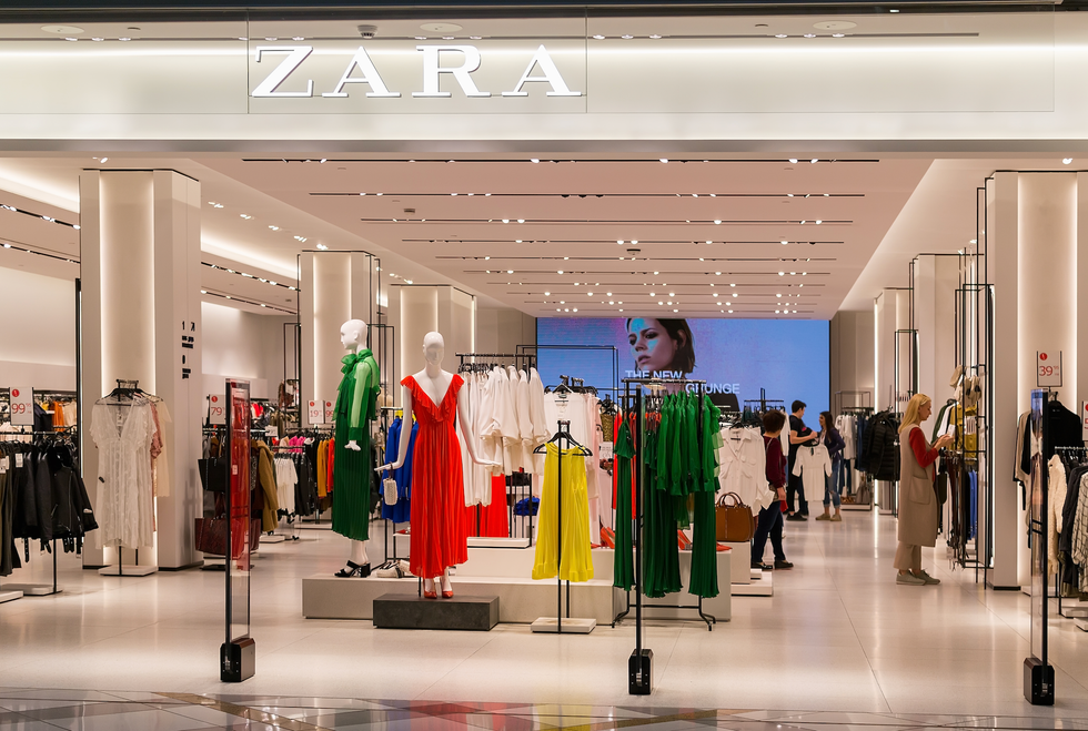 An exterior shot of a Zara store, showing racks of clothes and mannequins.
