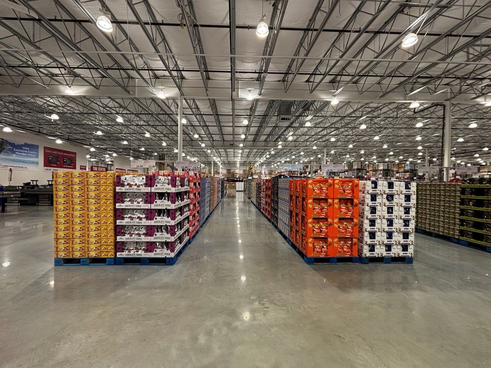 An interior aisle of the new Brantford Costco, lined with bulk-packaged snacks, shows the store\u2019s vast layout and high ceiling illuminated with bright lights.