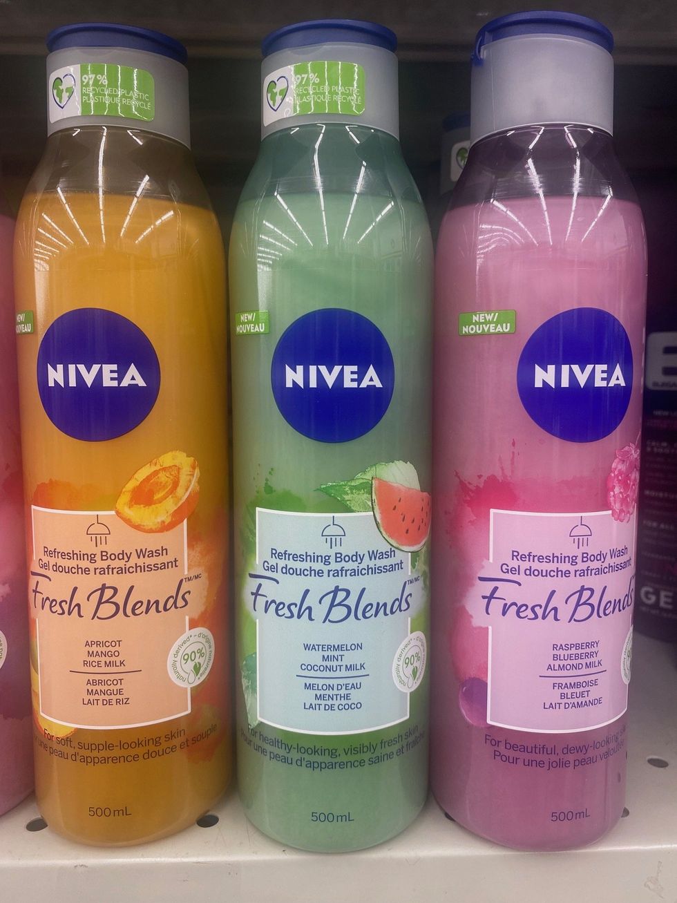 An orange bottle, green bottle and pink bottle of body washes on a store shelf.