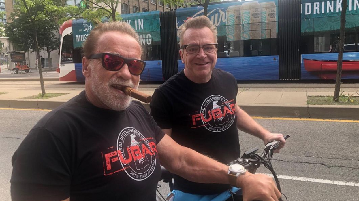 Arnold Schwarzenegger and Tom Arnold wearing "FUBAR" shirts while cycling in Toronto.