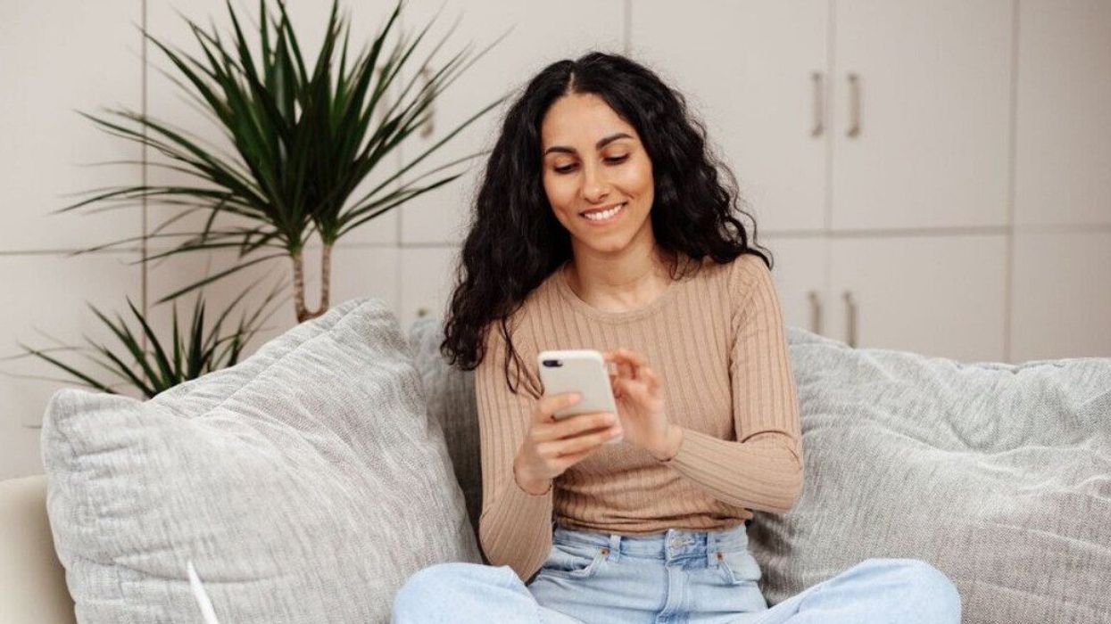 Assise sur un canapé, une jeune femme utilise son téléphone.